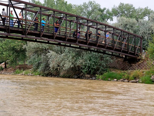 Onlookers view the Animas River from a bridge as orange