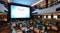 A large open seating area at the base of the atrium on Deck 6 faces a giant screen that is used to show live sporting events and other entertainment.