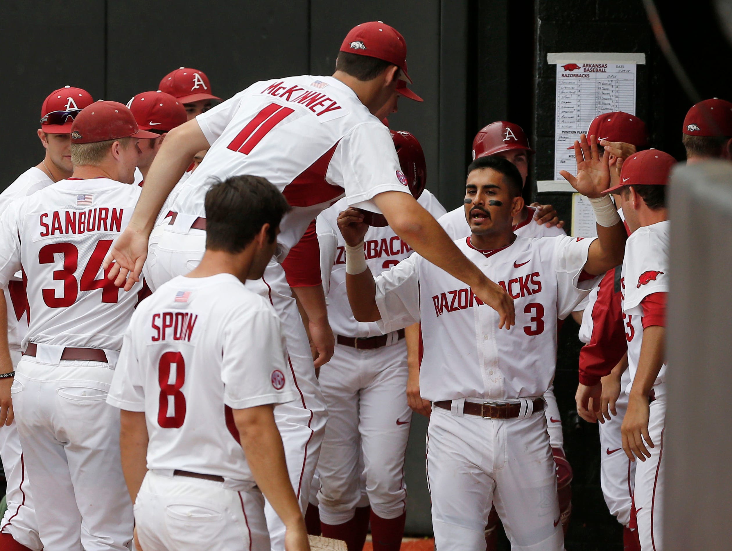 Arkansas’ Keaton McKinney (11) and Tyler Spoon (8) congratulate Michael Bernal, right, in the dugout after Bernal scored on a single by Tucker Pennell in the third inning of Friday’s regional game against Oral Roberts.