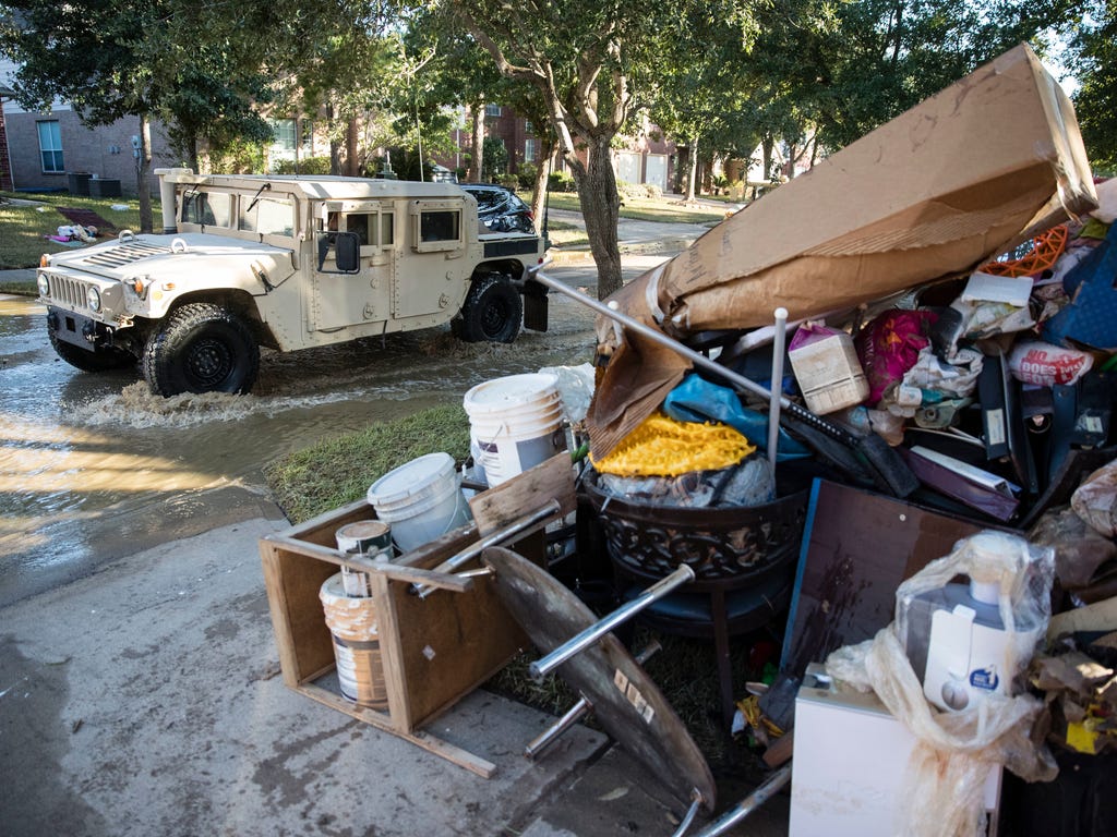 A military vehicle passws flood damaged belongings piled on a homeowners front lawn in the aftermath of Hurricane Harvey in Katy, TX.