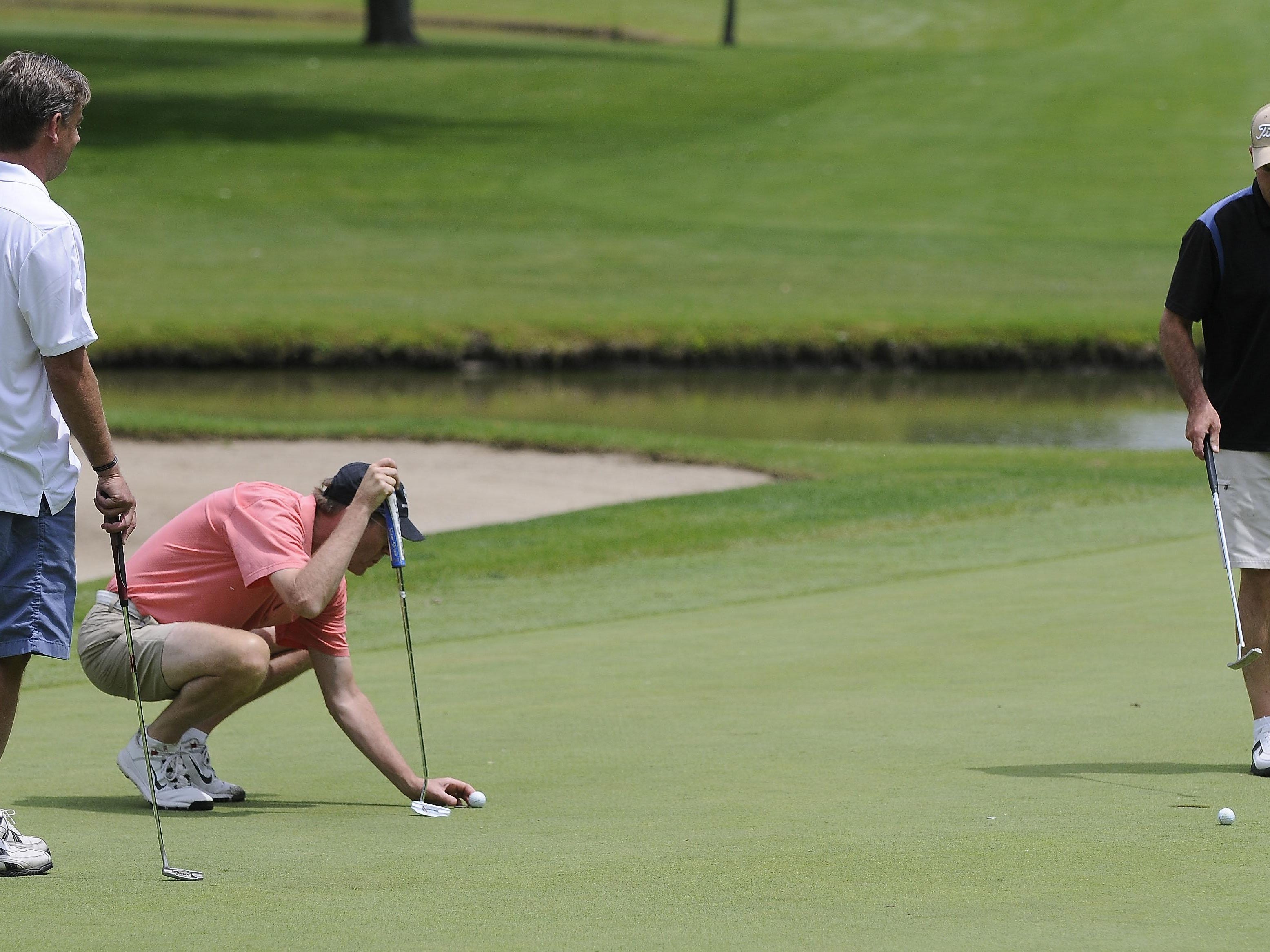 Mike Cansfield places his ball on the 18th hole as Rob McNeill, left, and Scot Smith look on during the Port Huron Elks 2015 Men's Invitational in Port Huron Township.