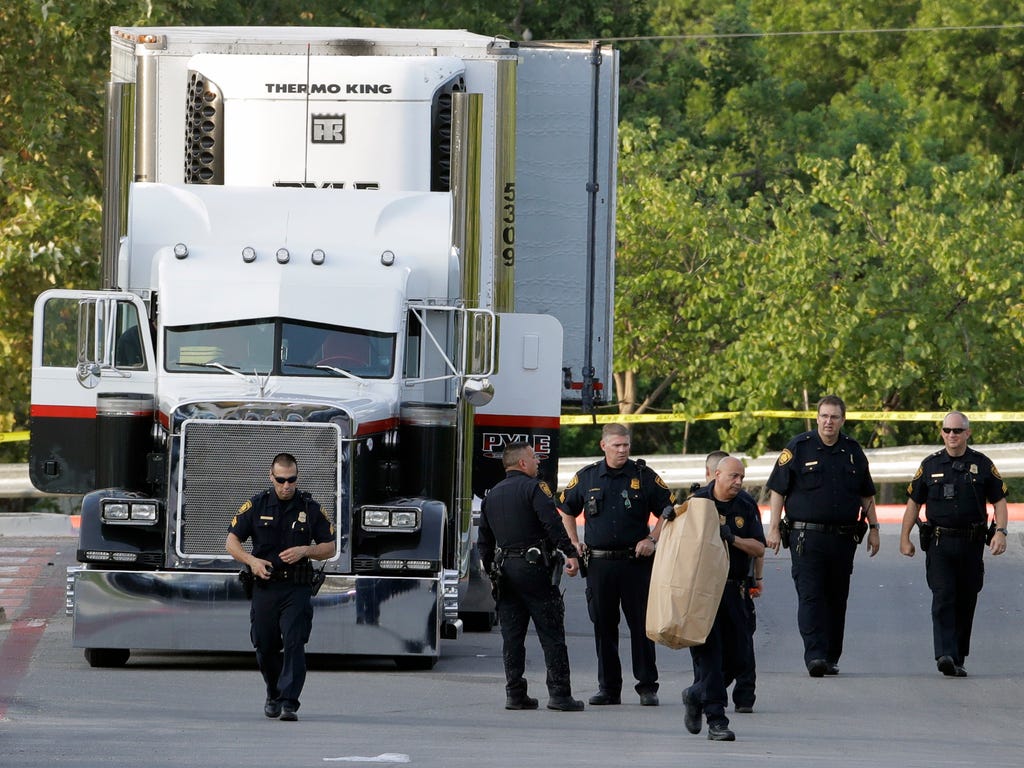 San Antonio police officers investigate the scene where eight people were found dead in a tractor-trailer loaded with at least 30 others outside a Walmart store in stifling summer heat in what police are calling a horrific human trafficking case in S