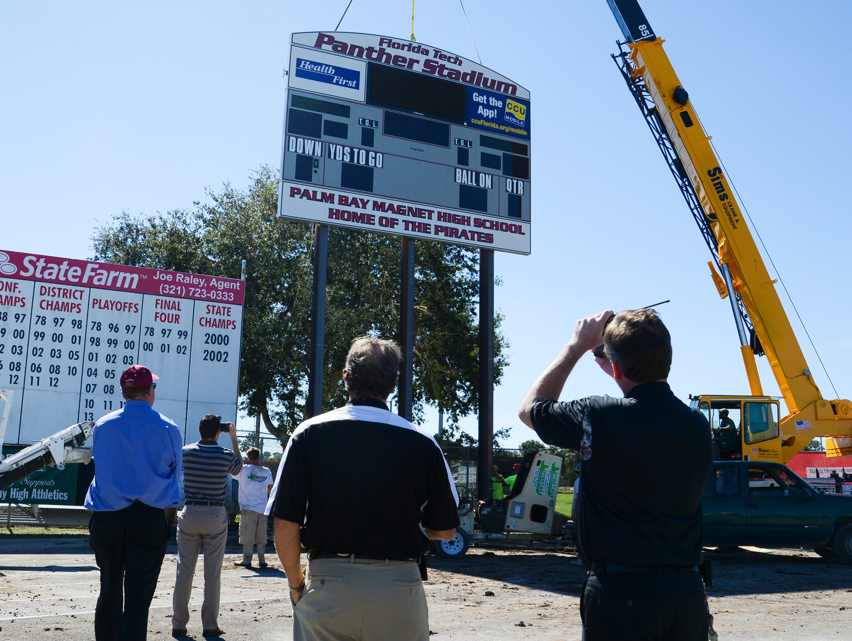 Officials from Florida Tech and Palm Bay High School watch as workers install the new scoreboard sign at Panther Stadium in Melbourne Friday.