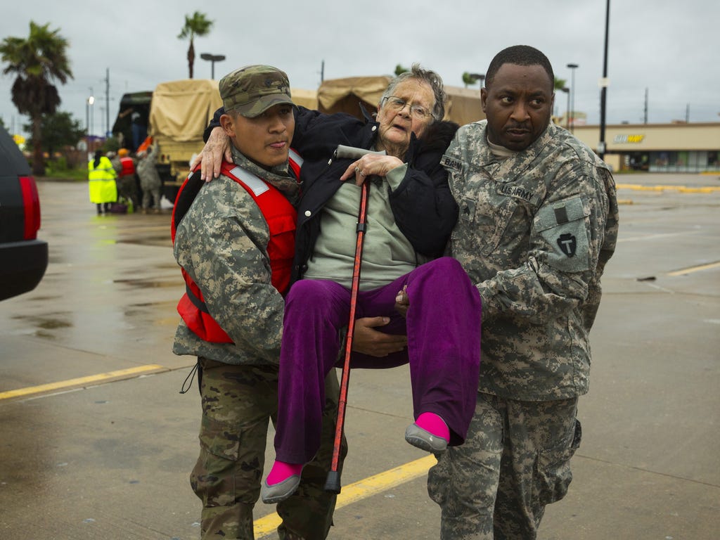 Texas Army National Guard members Sergio Esquivel, left, and Ernest Barmore carry 81-year-old Ramona Bennett after she and other residents were rescued from their Pine Forest Village neighborhood due to high water from Hurricane Harvey Aug. 29, 2017,