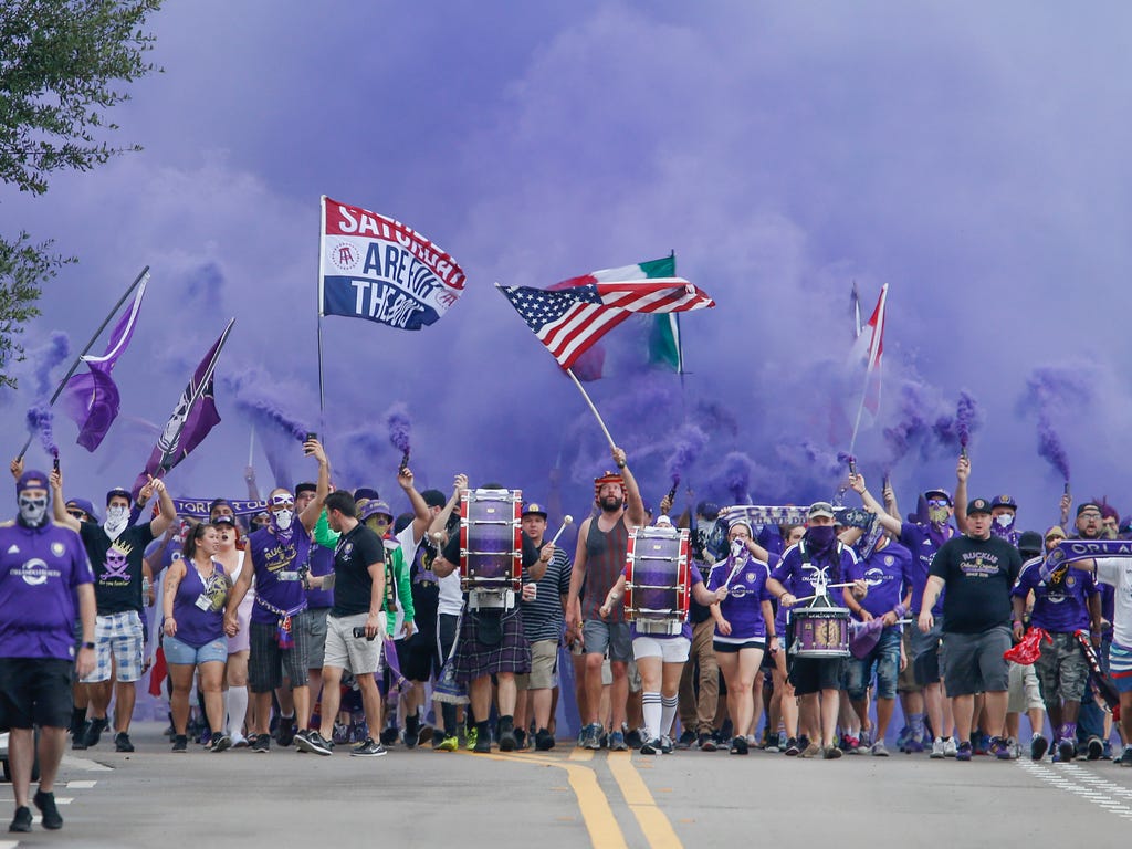 Orlando City SC fans march to the stadium waving banners and flags under a canopy of purple smoke before a match against the Vancouver Whitecaps at Orlando City Stadium.