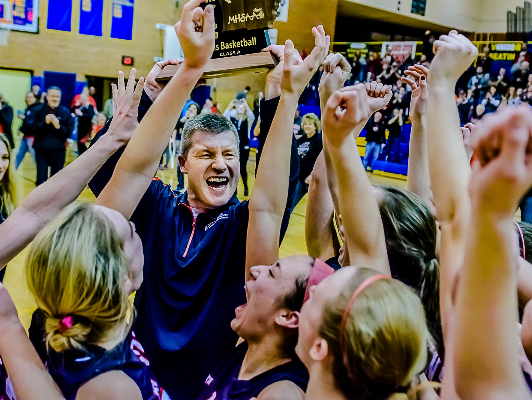 St. Johns Girls Basketball Head Coach Mark Lasceski ,center, raises the Class A regional trophy as he celebrates with his team after their win over Saginaw Heritage Thursday March 10, 2016 at Midland High in Midland. KEVIN W. FOWLER PHOTO