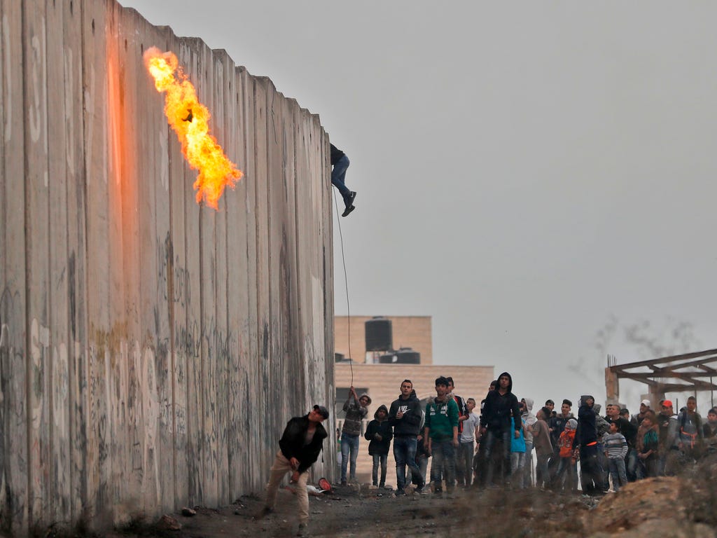 Palestinians throw a molotov cocktail and stones towards Israeli forces on the other side of a barrier at the Qalandia checkpoint in the occupied West Bank on Dec. 20, 2017, as protests continue following the President Trump's controversial recogniti