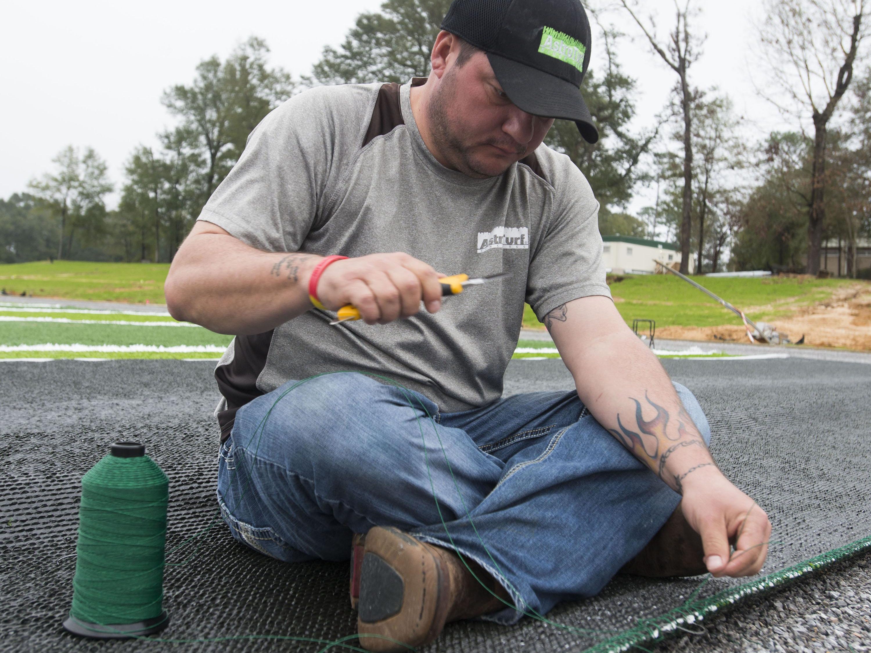 Brandon Curtis hand-stitchs a section of AstroTurf together during the installation of the new playing surface at University of West Football facility Friday morning Jan. 8, 2016.