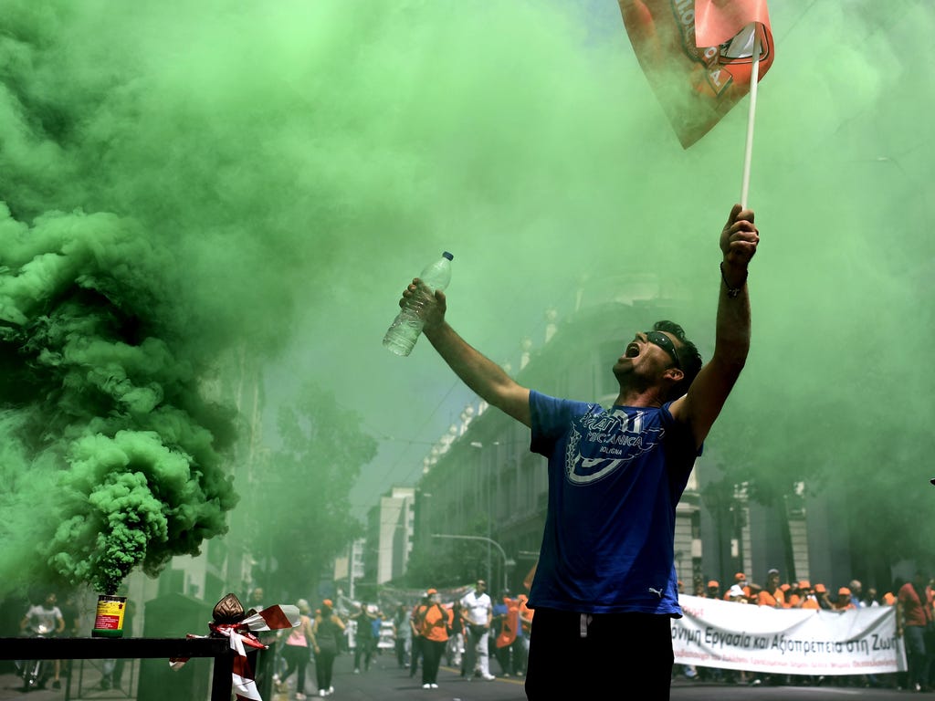 A contract municipal worker holds a flag next to a green smoke flare and shouts at the entrance to the Greek parliament in Athens during a protest.