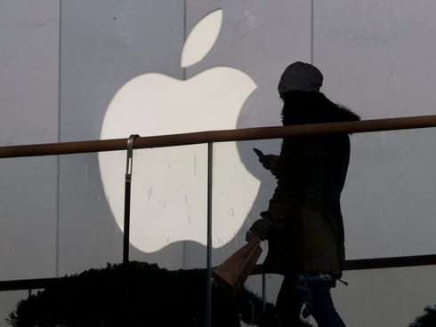 A woman using a phone walks past Apple's logo near its retail outlet in Beijing in Dec. last year.