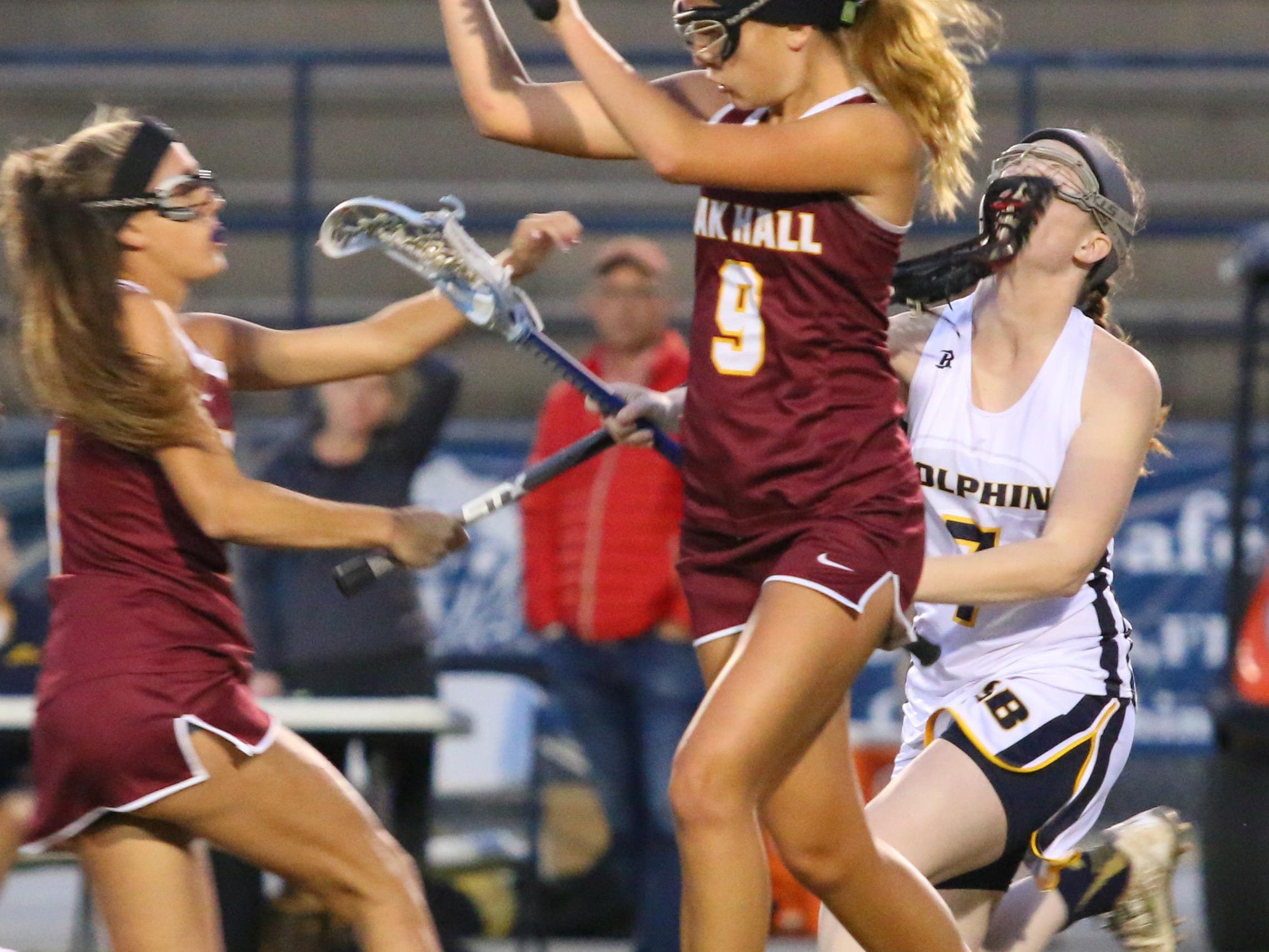 Gulf Breeze's E. Libby McDowell, right, gets hit in the face by the stick of Oak Hall's Emma Johnson, left, as Johnson's teammate Ashton Avera goes by them Friday night during the Region 1-1A lacrosse first round play-in game at Gulf Breeze High School.