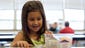 Caroline Nethery, 6, opens her boxed lunch at Bates Elementary School. All students at 95 schools across Jefferson County Public Schools will be allowed to eat both breakfast and lunch for free starting this fall, under an agreement between the district and the U.S. Department of Agriculture and the National School Lunch Act. June 9, 2014.