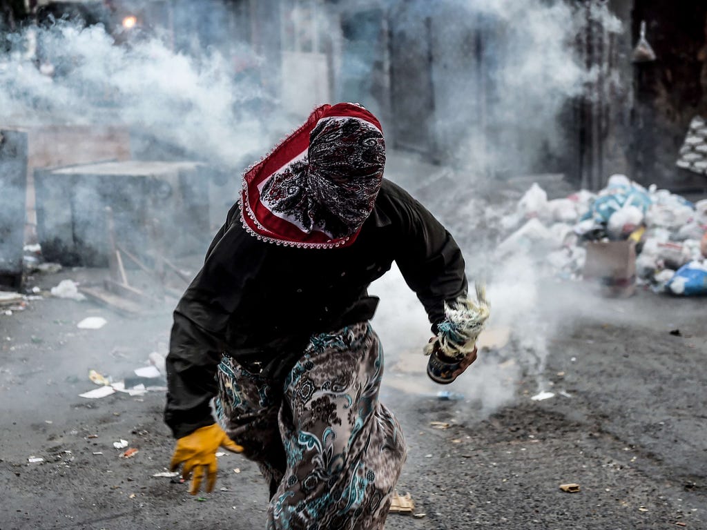 A masked Kurdish militant holds a molotov cocktail while he runs away from a tear gas cannister during clashes with Turkish police in the Gazi district of Istanbul.