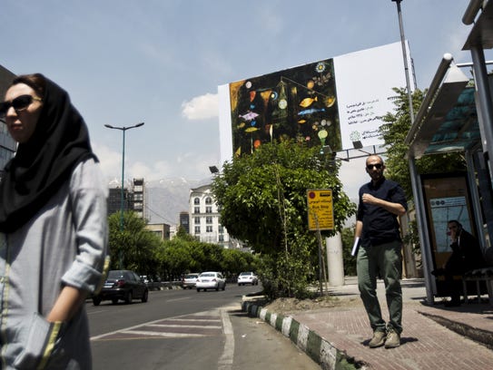 Iranians wait at a bus station next to a billboard