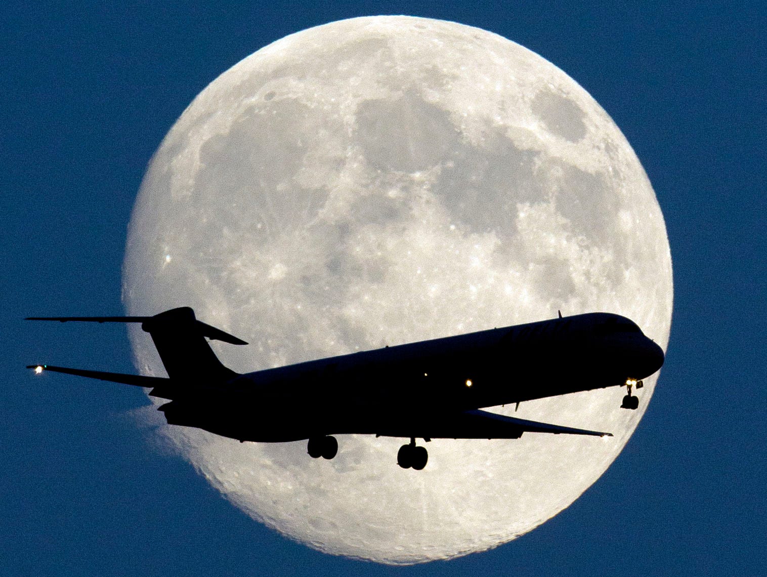 An airplane passes a nearly full moon as it  approaches Philadelphia International Airport on Sept. 7, 2014.