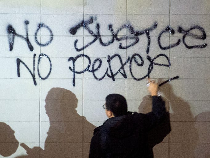 A demonstrator paints protest graffiti in Oakland,