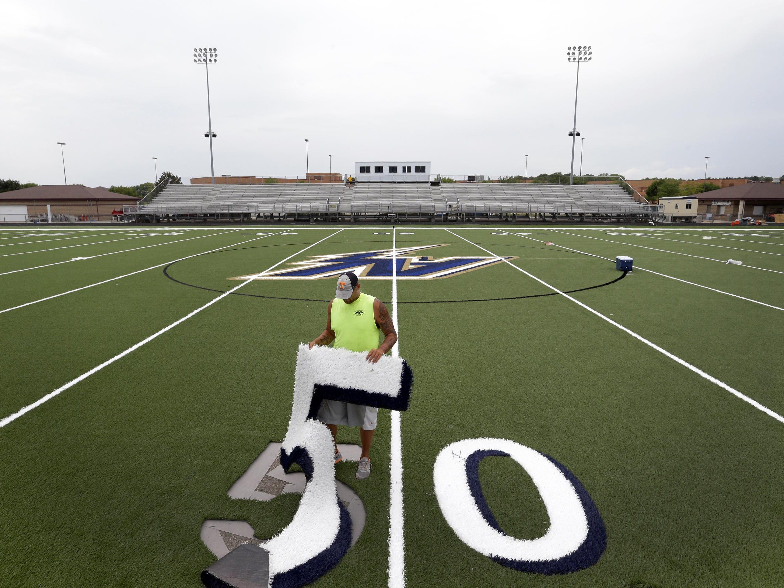 After setting seam tape in preparation for a glue application, Sports Contracting Group employee Sean Young puts a 50-yard mark in place on the new artificial turf Monday at Appleton North High School.
