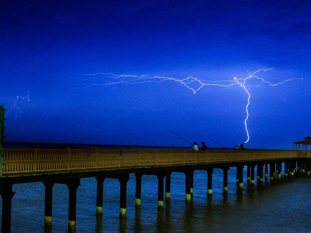 Lightning flashes over people fishing on the coast near Kuwait City, Kuwait.