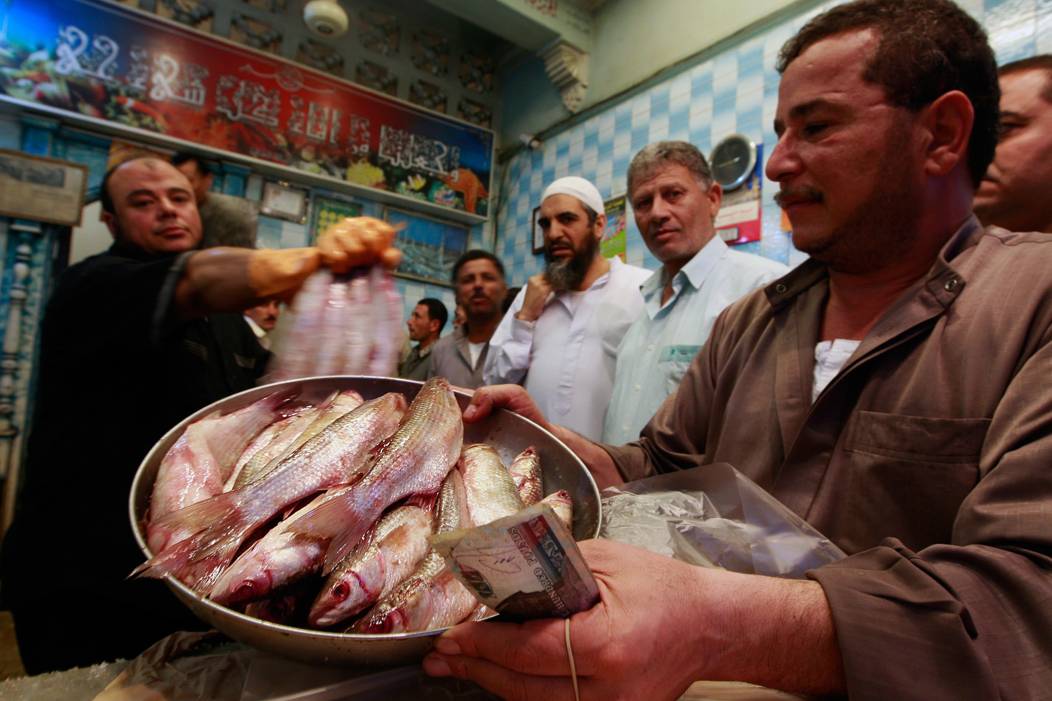 Shop owner Ehab el-Yamani, left, sells a fish dish
