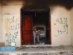 A man looks at documents at the U.S. consulate in Benghazi, Libya, after an attack that killed four Americans. The graffiti reads, "no God but God,"  "God is great," and "Mohammed is the Prophet."
