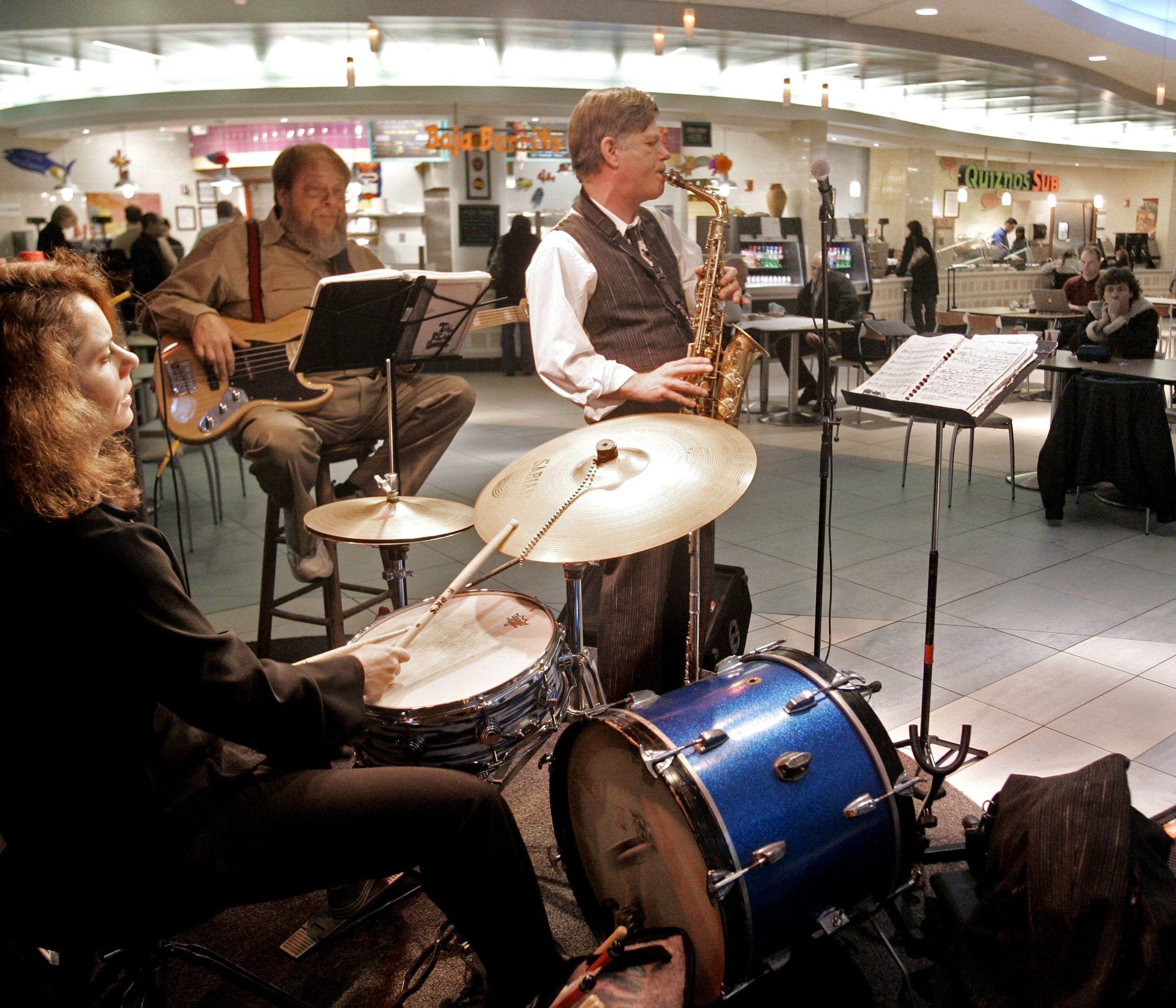Drummer Kelly Bamberger, bass player Gary Branchaud, and saxophonist John Heinrich perform in a food court at the Nashville International Airport.