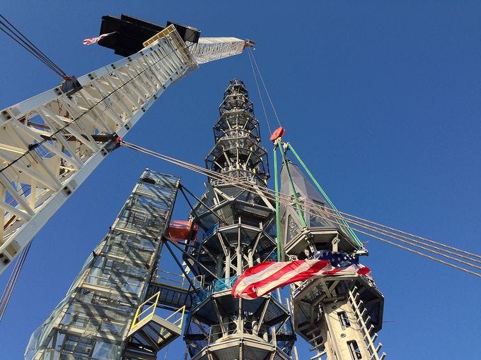 An American flag is draped on the spire as workers prepare to raise the structure.