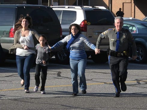 In this Dec. 14 photo provided by the Newtown Bee, a police officer leads two women and a child from Sandy Hook Elementary School in Newtown, Conn., shortly after Adam Lanza opened fire, killing 26 people, including 20 children.