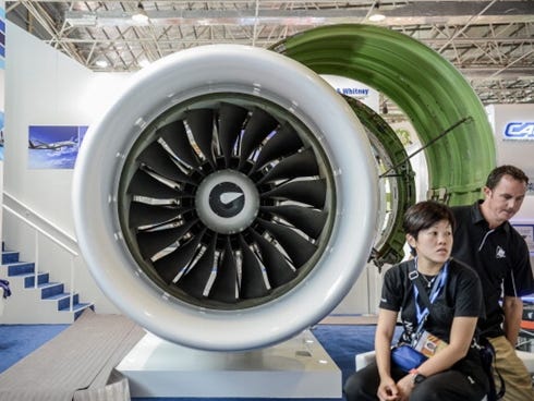 Exhibitors sit next to a jet engine at the Pratt and Whitney booth on the eve of the 2012 China International Aviation and Aerospace Exhibition in Zhuhai.