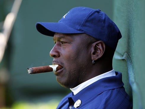 Michael Jordan watches golf and smokes a cigar.
