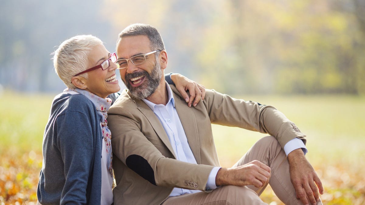 Two seniors sitting on ground outdoors and laughing.