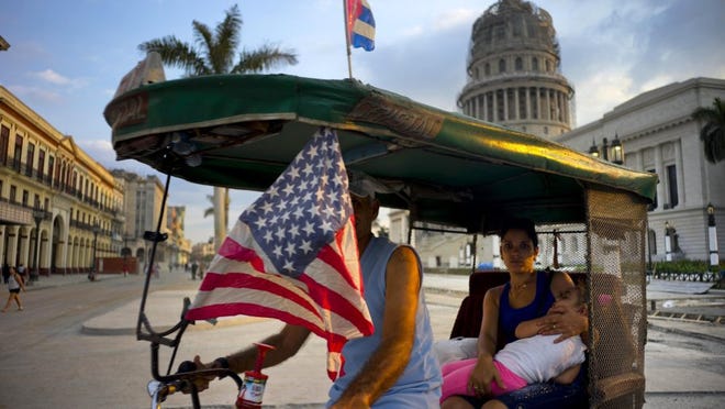 A taxi pedals his bicycle, decorated with Cuban and U.S. flags, as he transports a woman holding a sleeping girl, near the Capitolio in Havana, Cuba, Tuesday, March 15, 2016. President Barack Obama will travel to Cuba on March 20. (AP Photo/Ramon Espinosa)