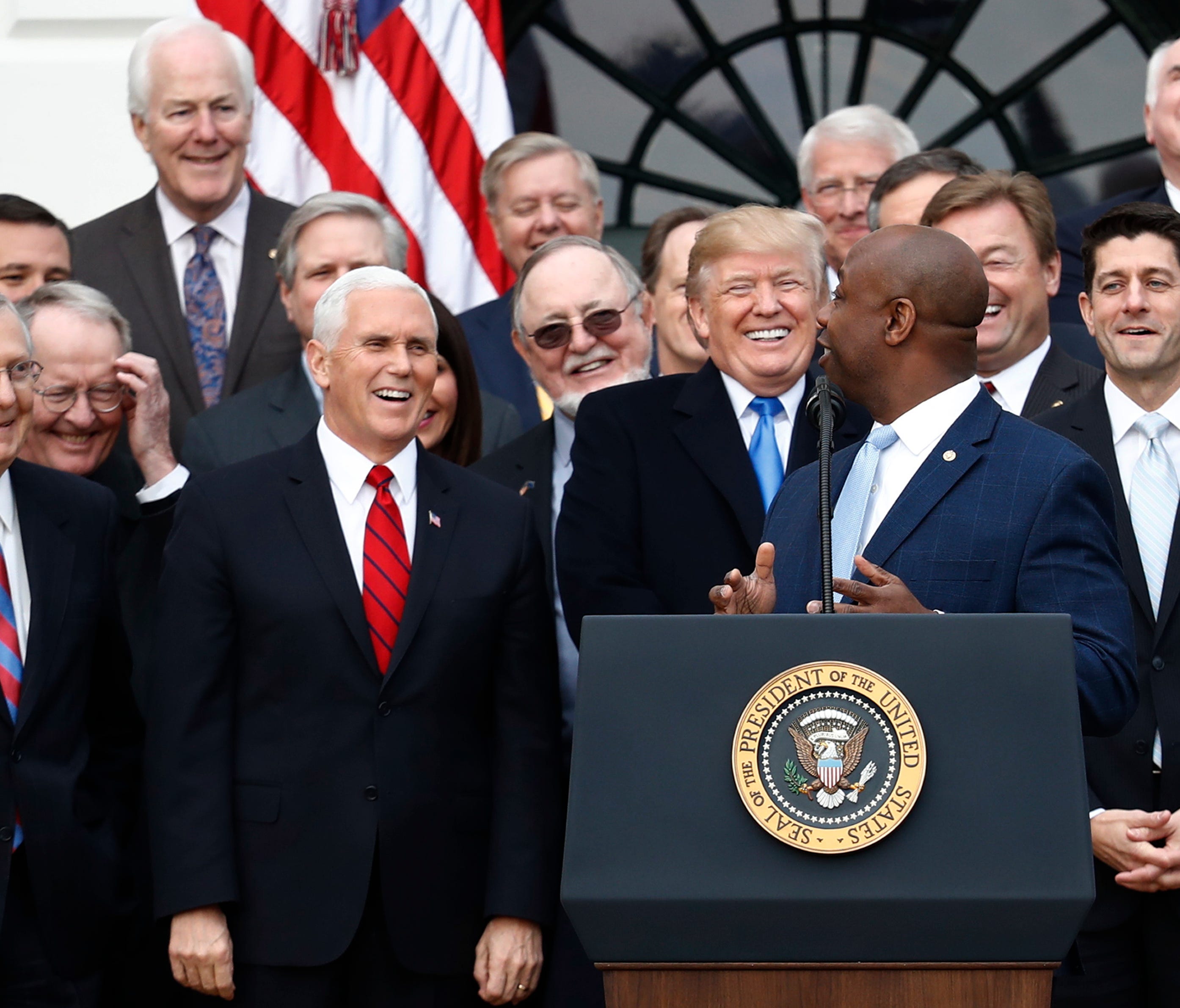 President Donald Trump smiles  with Senate Majority leader Mitch mcConnell of Ky., Vice President Mike Pence and House Speaker Paul Ryan of Wis., as Sen. Tim Scott, R-S.C., speaks during a bill passage event on the South Lawn of the White House in Wa
