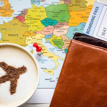 A world map with a wallet, plane tickets, and cup of coffee with airplane shape made of cocoa powder floating on top of the coffee.