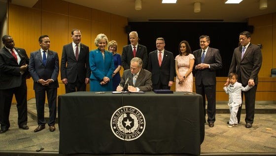 Texas Gov. Greg Abbott signs into law that would overhaul the state's child welfare system. Rep. James Frank, back and center, and other legislators who worked on the bills watch as their endeavor becomes reality.