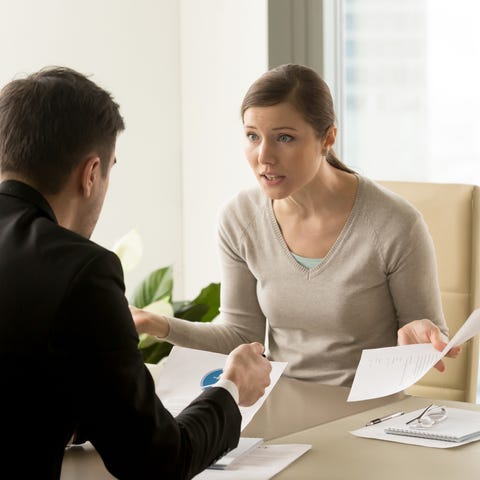 In an office setting, a woman holding papers sits 