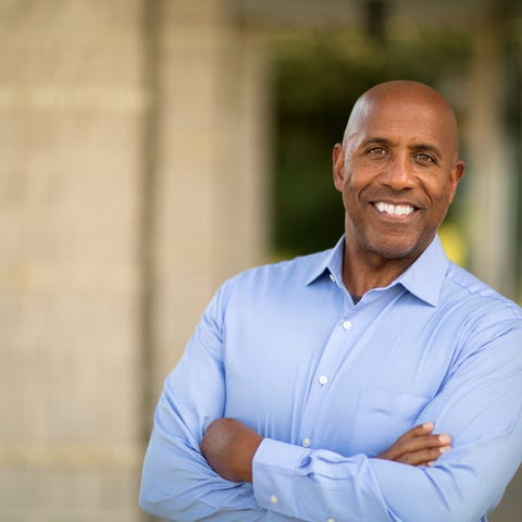 Smiling man in dress shirt standing with arms...