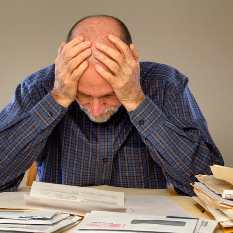 Older man holding his head while looking at papers