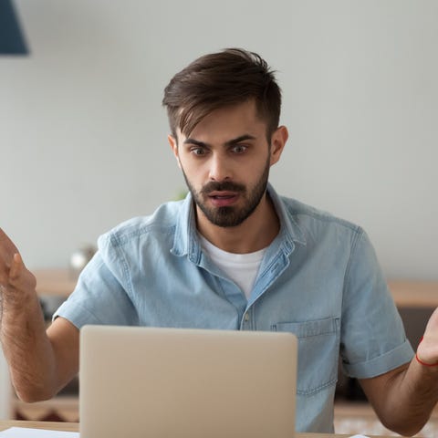 Wide-eyed office worker shrugs at his laptop.