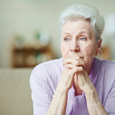 Senior woman sitting on a couch looking worried.