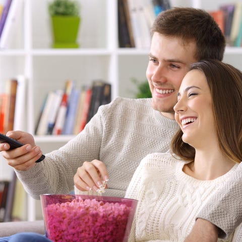 A similing young couple share popcorn in front of 