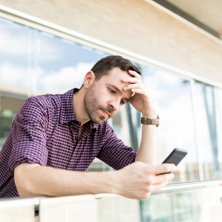 Man with worried expression holding head while looking at mobile phone