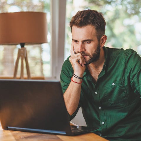 Man with a serious expression sits at laptop.