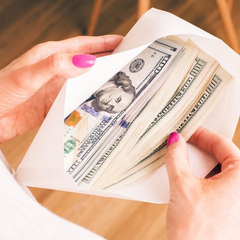 Older woman holding envelope full of $100 bills.