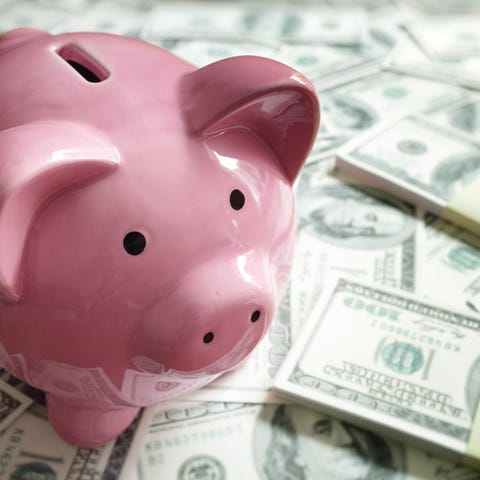 A piggy bank on top of hundred dollar bills spread