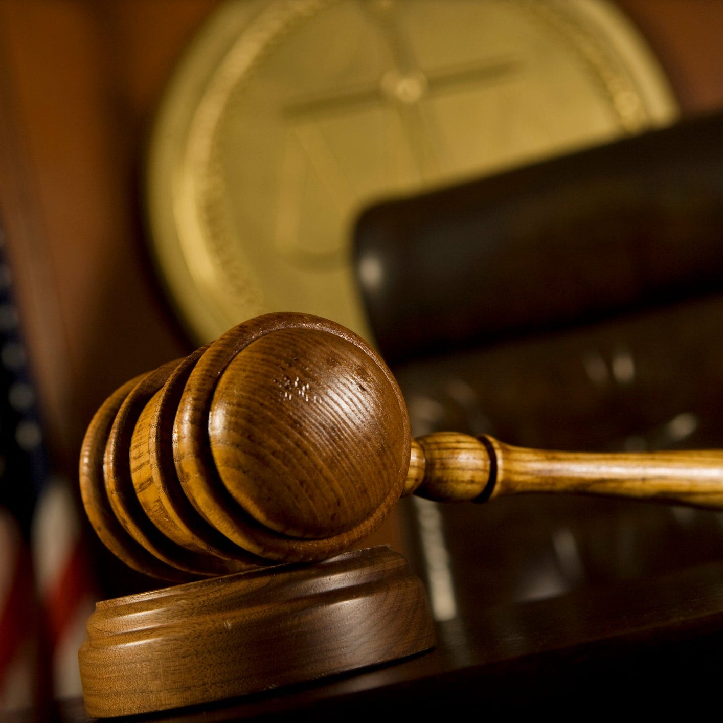A judge's gavel in the foreground, with a chair, court seal, and an American flag in the background.
