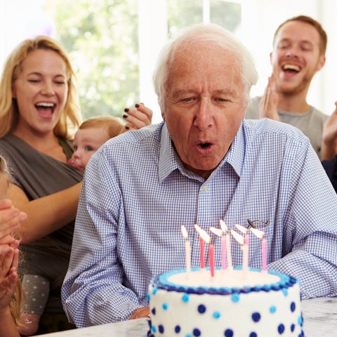 Older person blowing out candles on cake while fam