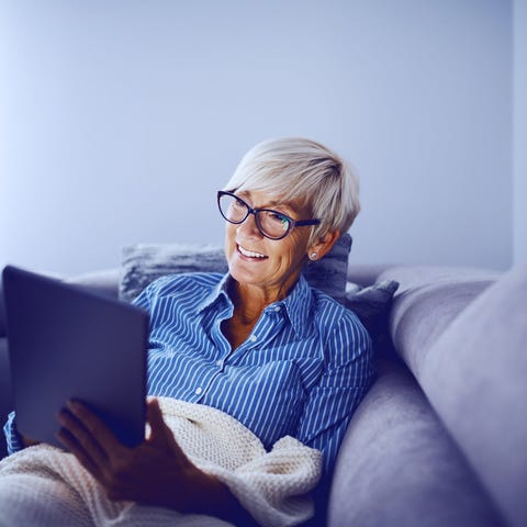Smiling older woman holding tablet on couch