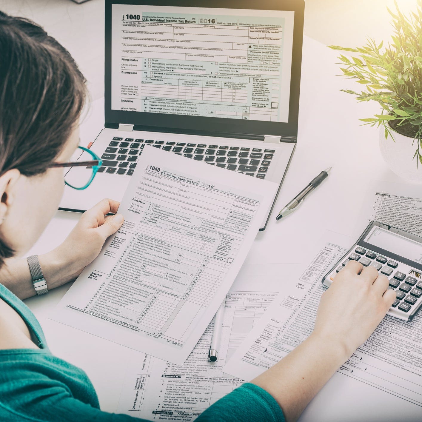 A woman looks at a tax return form and uses a calculator.