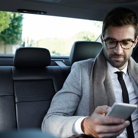 A businessperson looking at his smartphone while driving in the back of a taxi cab.