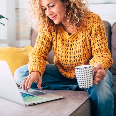 Smiling woman holding mug and looking at laptop